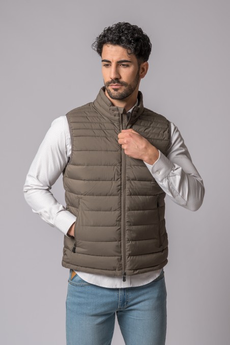 Homem a usar colete castanho acolchoado sobre camisa branca e calças de ganga