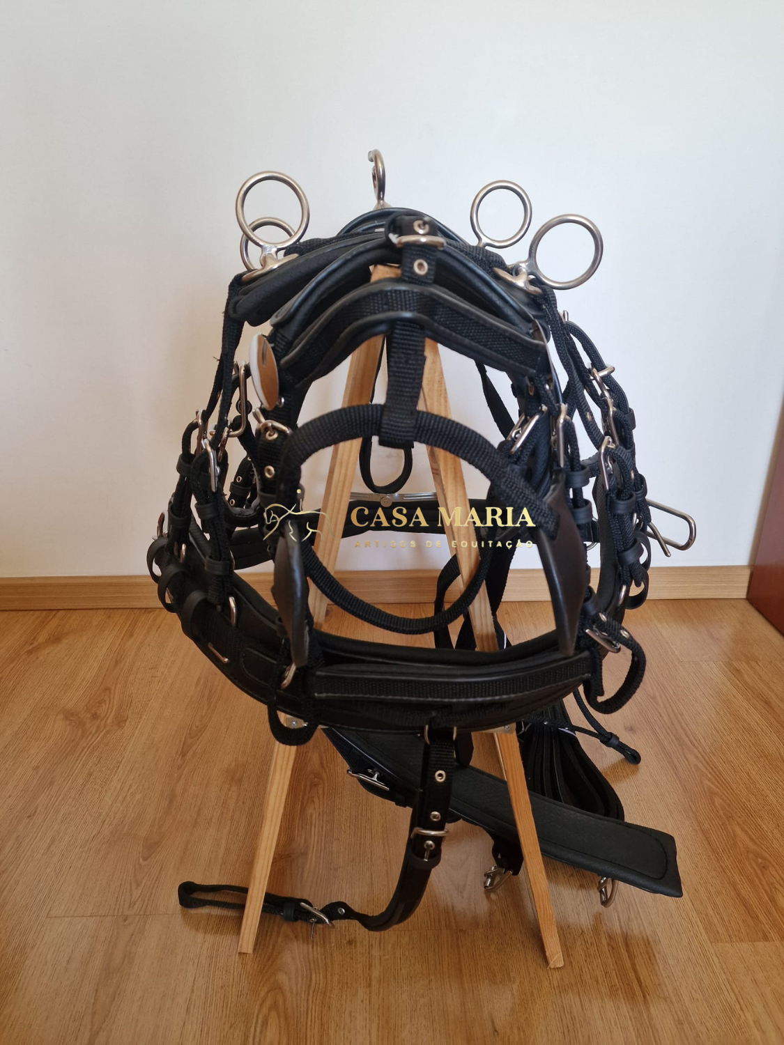 Arnês de equitação preto com anéis metálicos sobre base de madeira