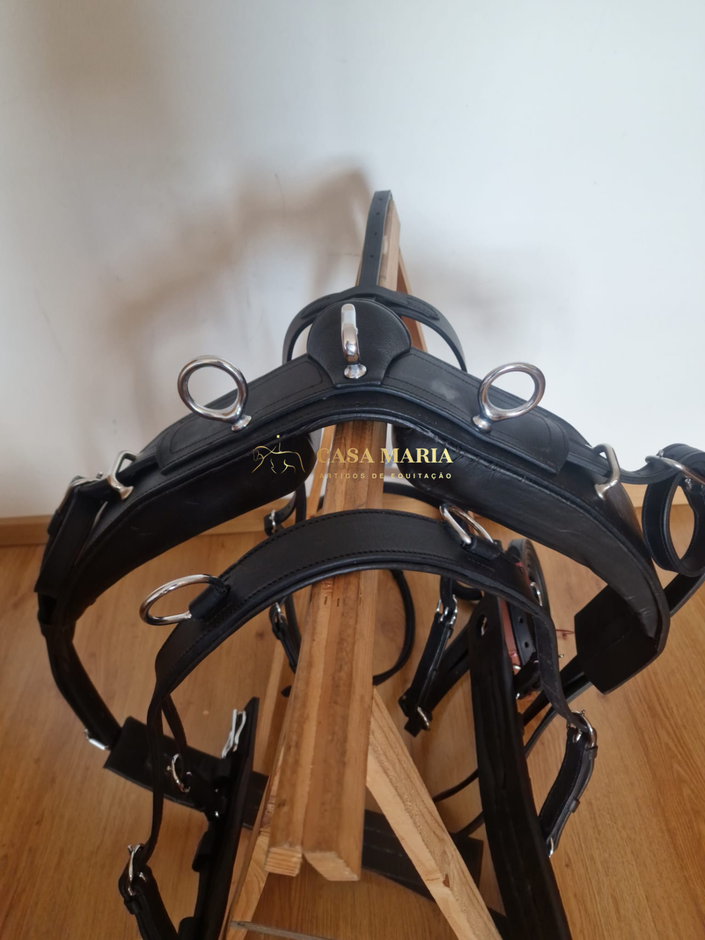 Arnês preto de couro com argolas metálicas num suporte de madeira