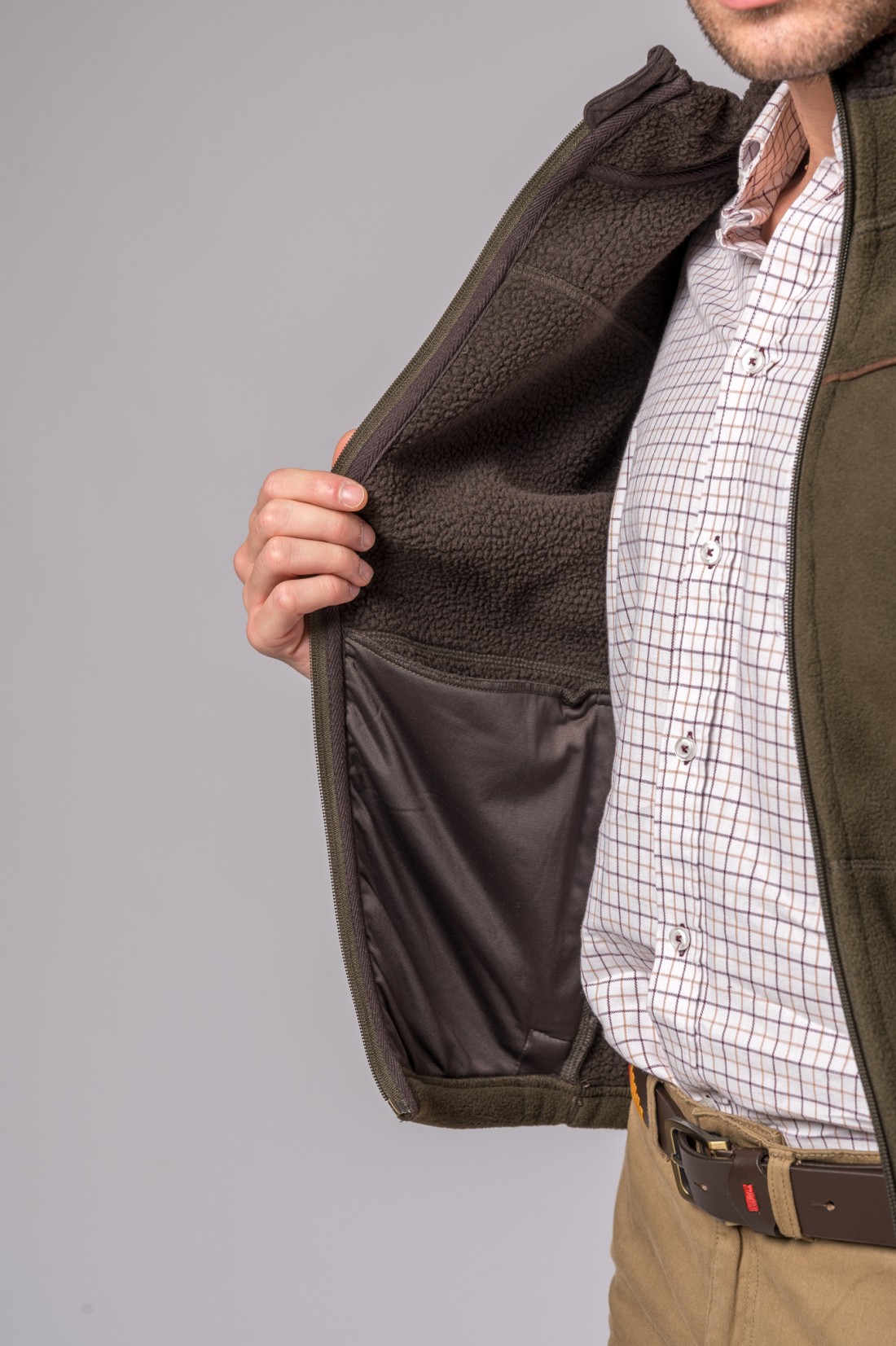 Colete verde oliva com interior em Sherpa castanho aberto mostrando forro castanho e pessoa com camisa quadriculada.