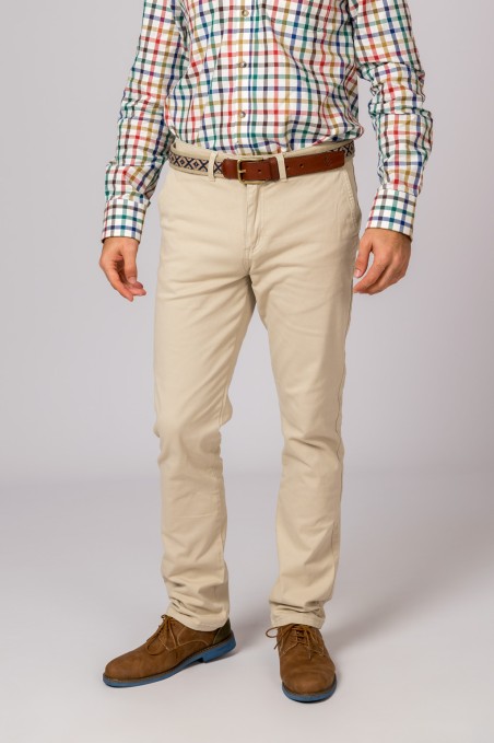 Homem com calças beige, camisa quadrada colorida, cinto castanho e sapatos castanhos.