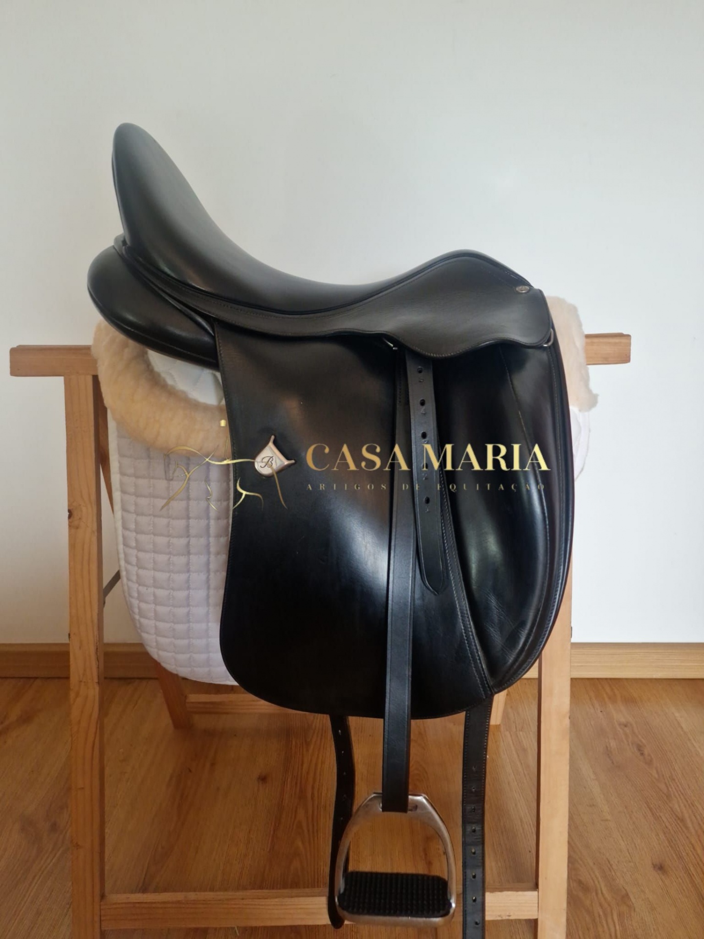 Sela de cavalo preta em couro com apoio branco sobre suporte de madeira