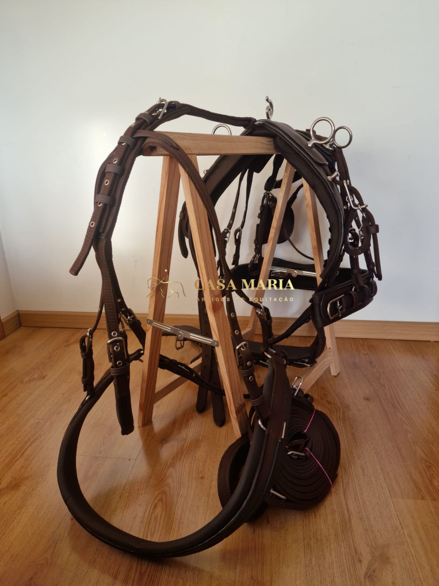 Bridão e rédeas de couro castanho com ferragens prateadas numa estrutura de madeira