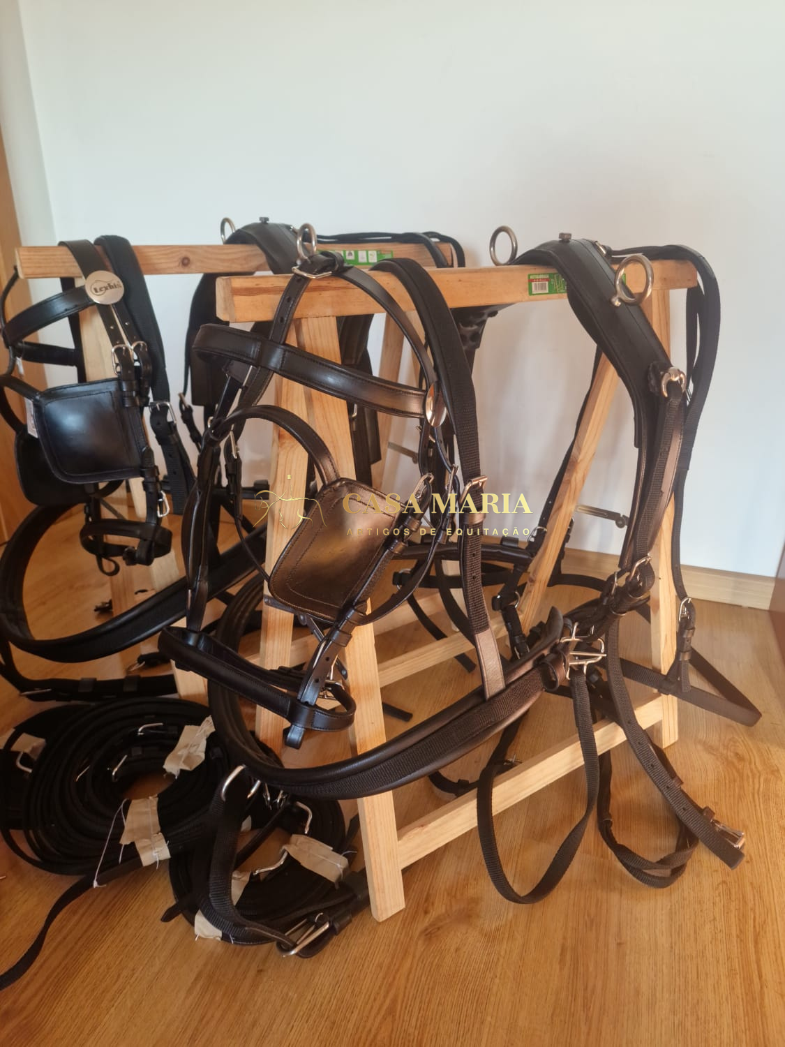 Arreios de couro preto com fivelas metálicas pendurados num suporte de madeira