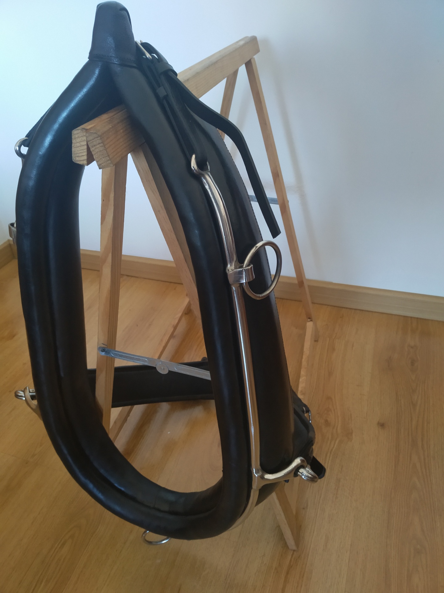 aparelho de equitação de couro preto com ferragens metálicas sobre suporte de madeira