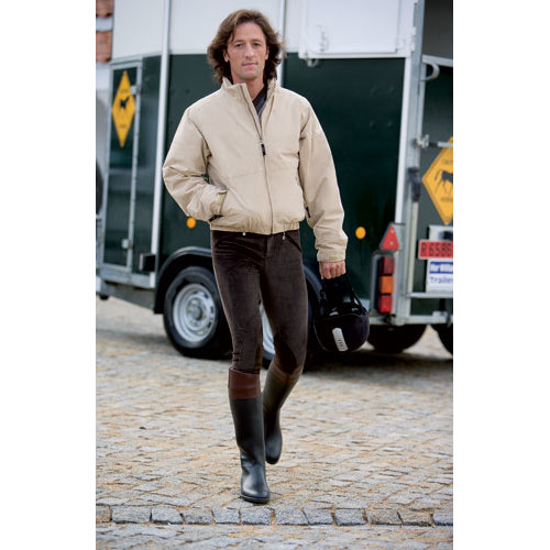 Homem com casaco bege, calças pretas e botas bicolores segurando capacete junto a carrinha.