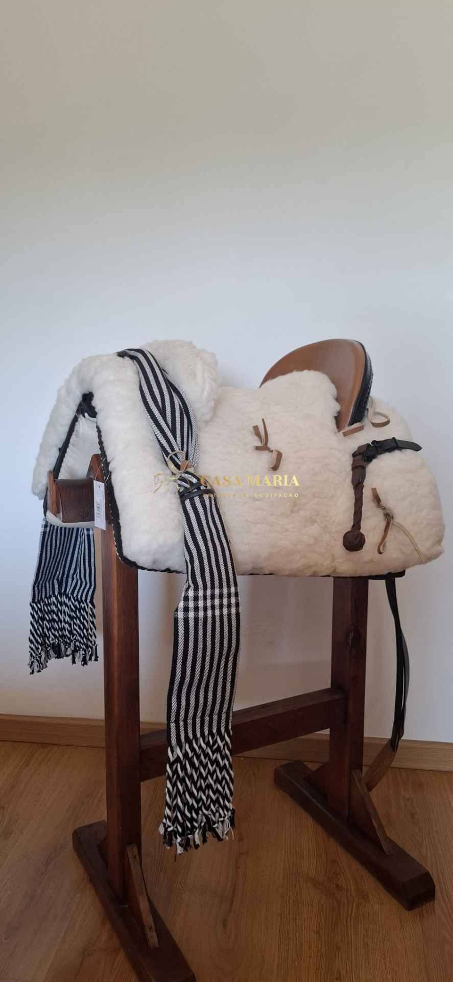 Sela de equitação com almofada branca e assento castanho em suporte de madeira