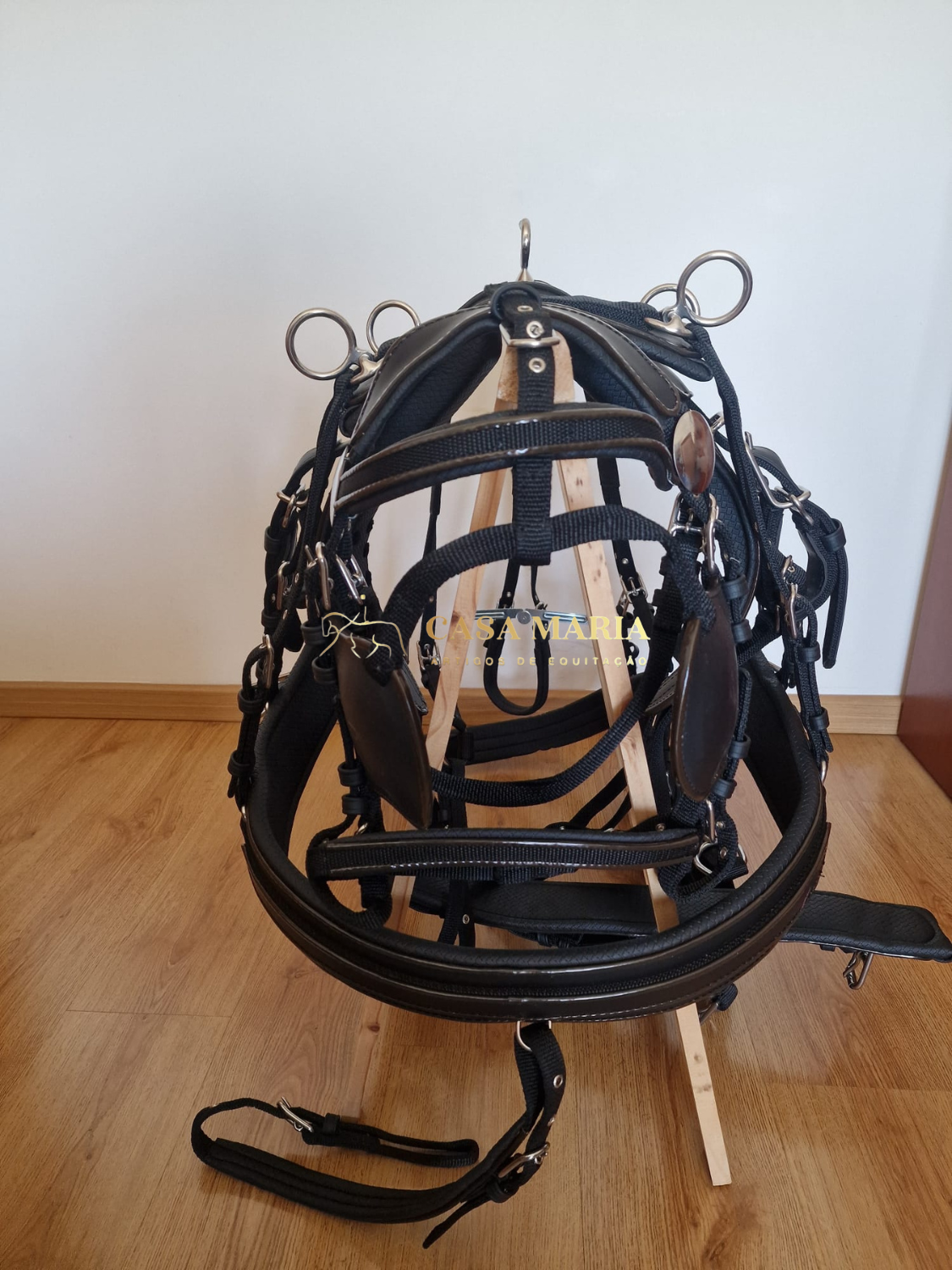 Peça de equipamento equestre preta com fivelas metálicas sobre estrutura de madeira