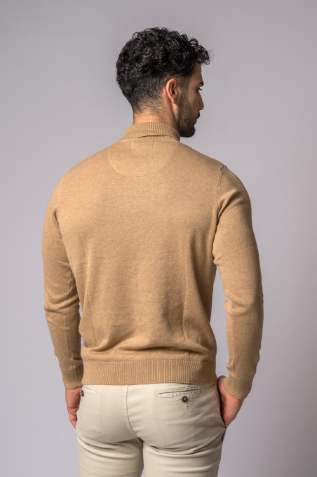 Homem com camisola castanha clara e calças bege visto de costas em fundo cinza claro