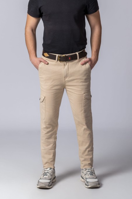 Homem vestido com calças cargo bege, cinto castanho, t-shirt preta e ténis cinza num fundo cinza claro