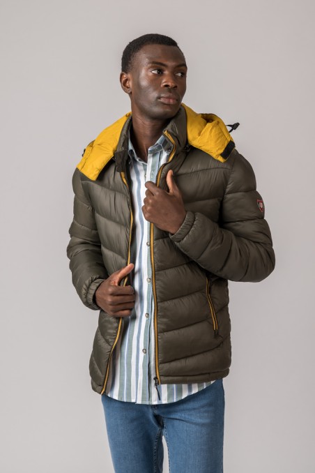 Casaco acolchoado verde-oliva com capuz amarelo e camisa de riscas azuis em modelo masculino