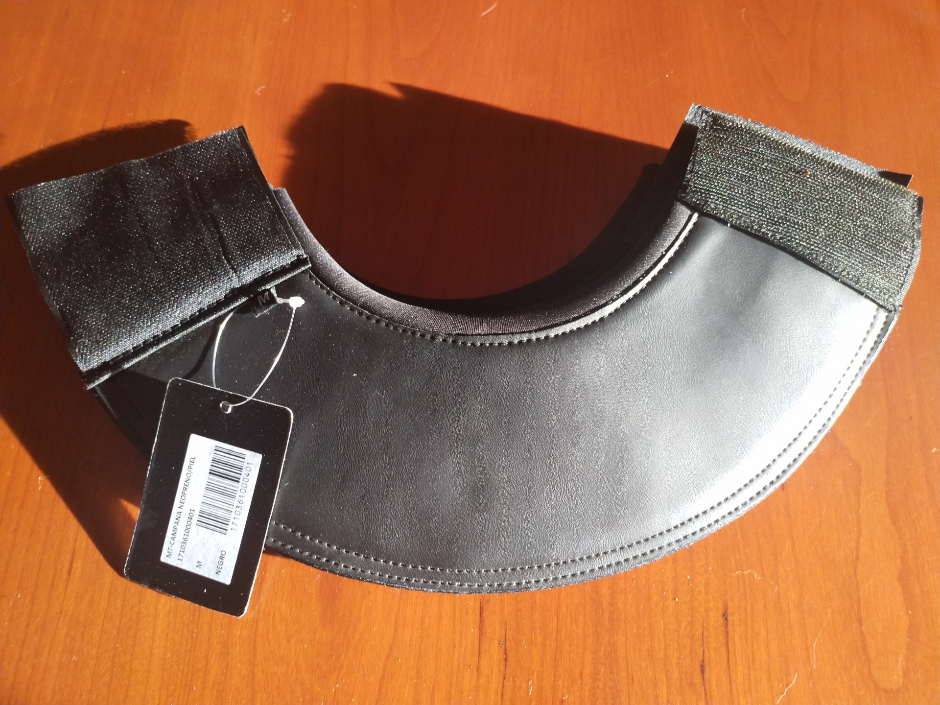 Proteção de ombros cinza com fechos de velcro pretos e etiqueta preta sobre mesa de madeira clara