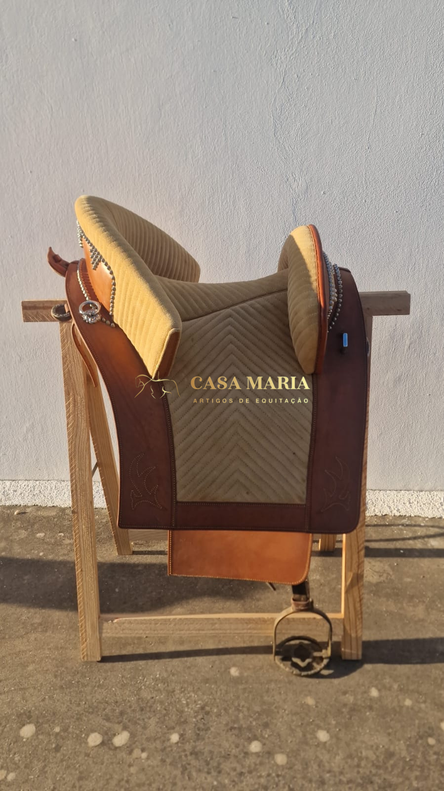 Sela de equitação em couro castanho e assento almofadado bege pendurada em suporte de madeira