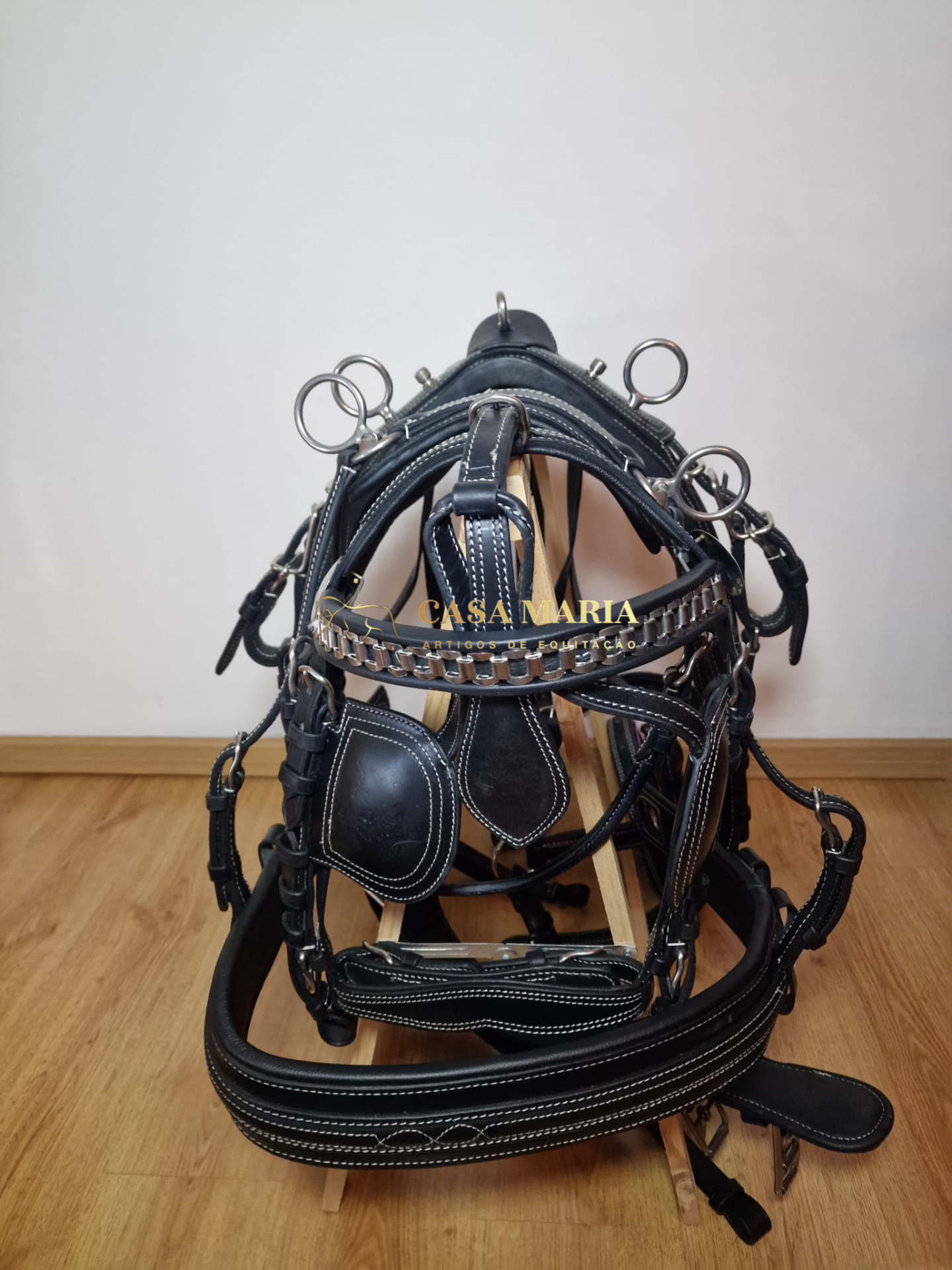 Bridão de cavalo em pele preta com detalhes metálicos sobre suporte de madeira