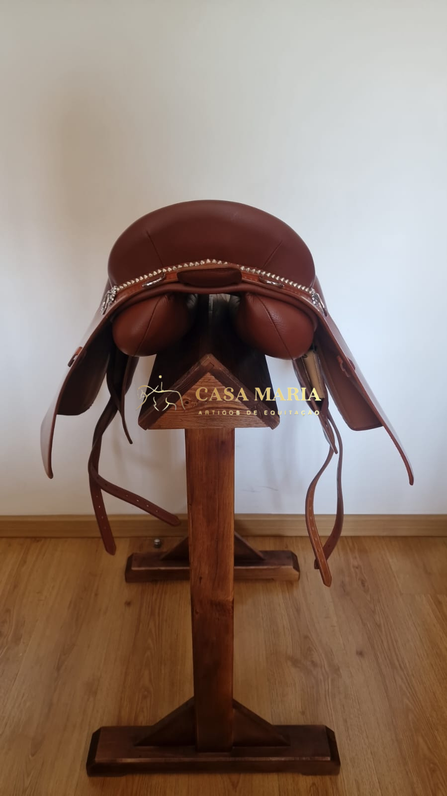 Sela de equitação castanha em couro com detalhes metálicos sobre suporte de madeira