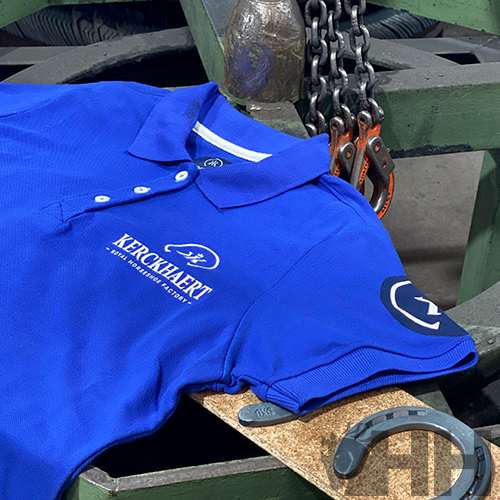 Polo azul com logotipos brancos 'KERCKHAERT' sobre equipamento metálico com correntes e ganchos