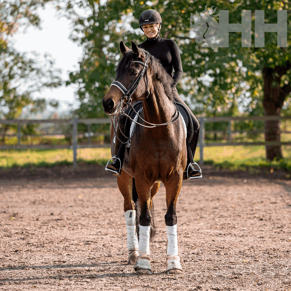 Pessoa a cavalgar um cavalo castanho com proteções brancas numa arena ao ar livre