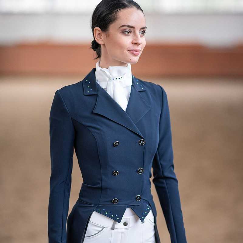 Mulher vestindo casaco de competição para equitação azul escuro e camisa branca, em ambiente interior de estábulo