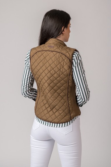 Colete feminino matelassê castanho visto de costas, usado com camisa riscas verticais e calças brancas.