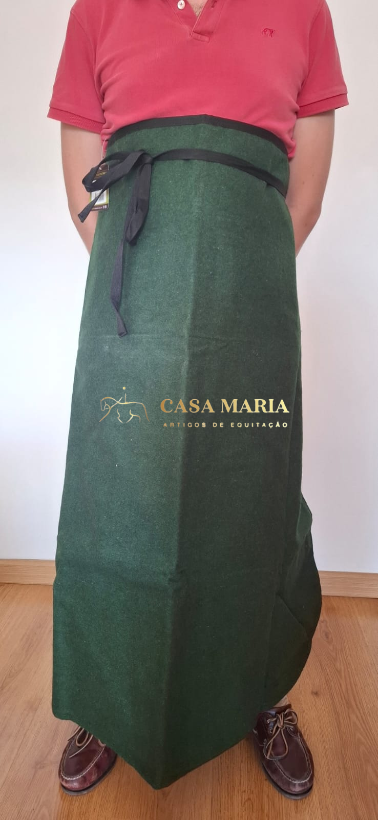 Pessoa com avental comprido verde escuro com fita preta, camisa polo vermelha e sapatos castanhos
