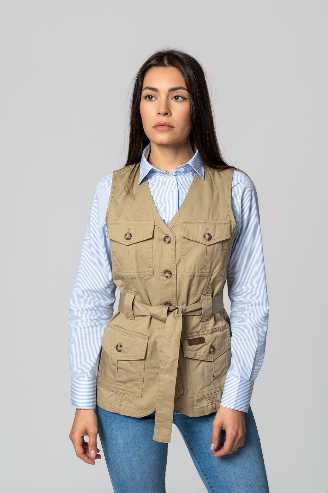 Mulher com colete bege e camisa azul clara às riscas com calças jeans azuis