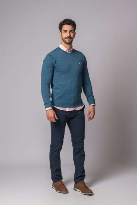 Homem com camisola azul e camisa rosa em fundo cinzento