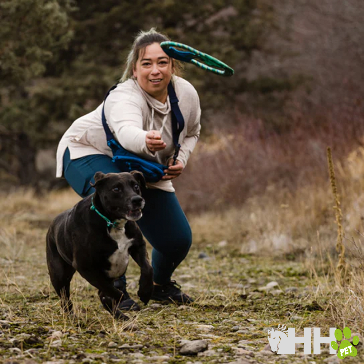 Mulher a lançar frisbee para cão preto ao ar livre numa área natural