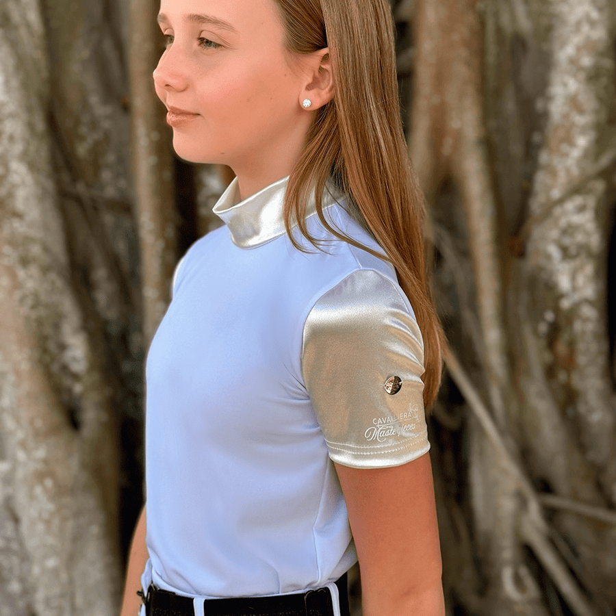 Camisa de manga curta azul claro com mangas prateadas e texto CAVALEIRA Masterpieces, usada por criança ao ar livre