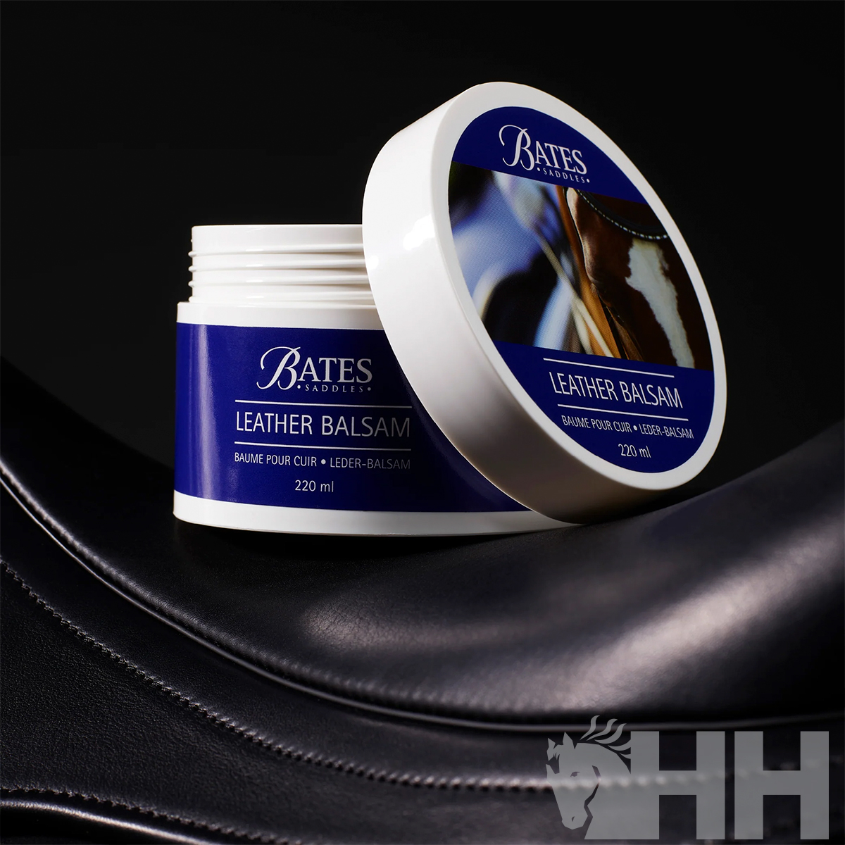 Frasco branco aberto de bálsamo para couro com rótulo azul da Bates Saddlery sobre couro preto