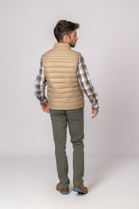 Homem de costas com colete bege acolchoado e camisa xadrez.