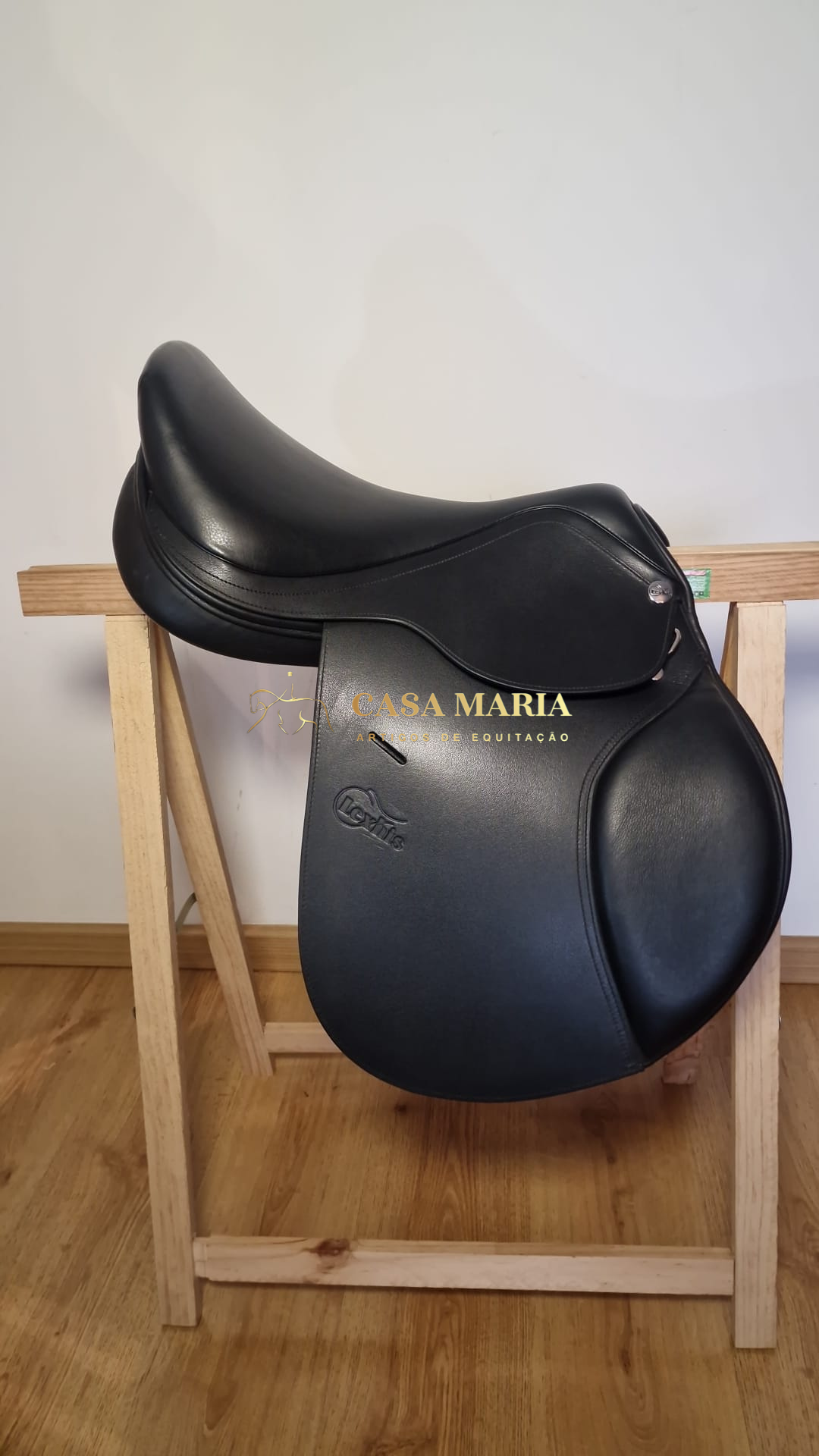 Sela de equitação preta em couro sobre suporte de madeira com texto CASA MARIA