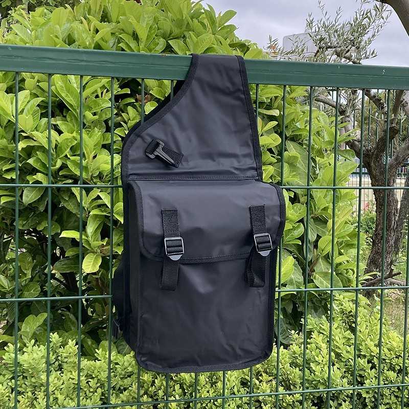 Mochila preta pendurada numa vedação verde com folhagem de fundo