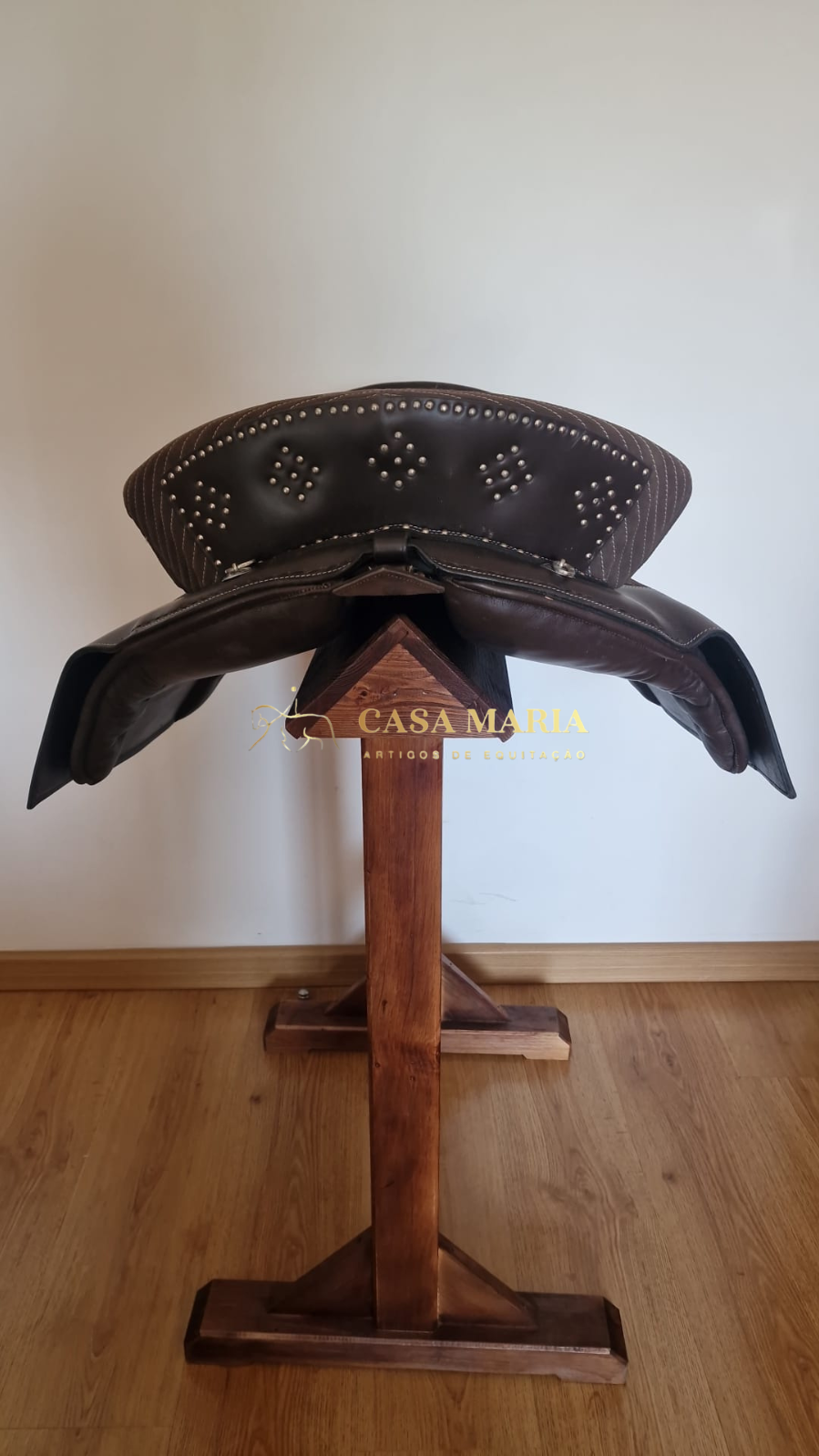 Sela de equitação castanha escura com tachas metálicas num suporte de madeira