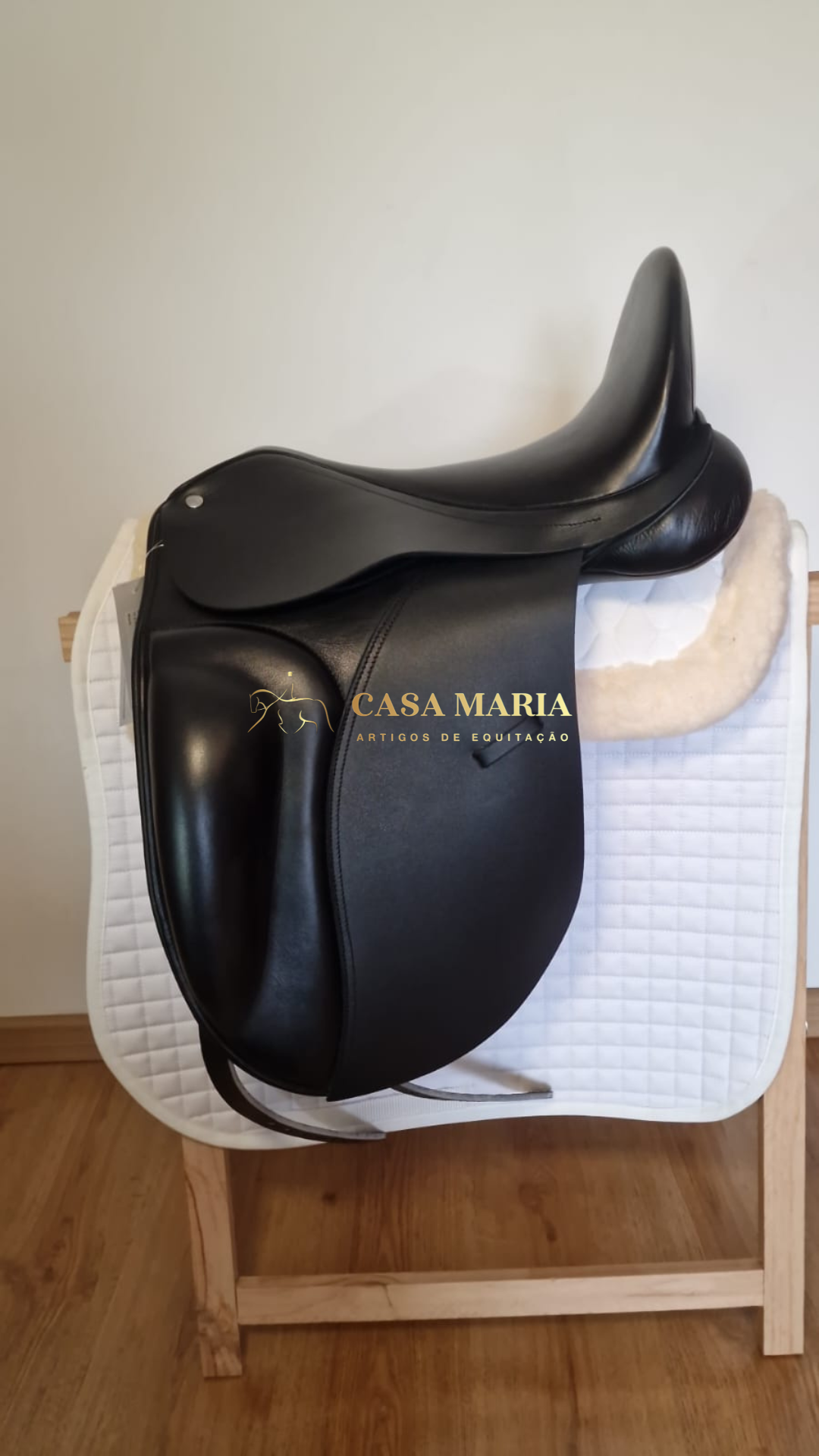 Selim de equitação preto em couro sobre almofada branca acolchoada e suporte de madeira