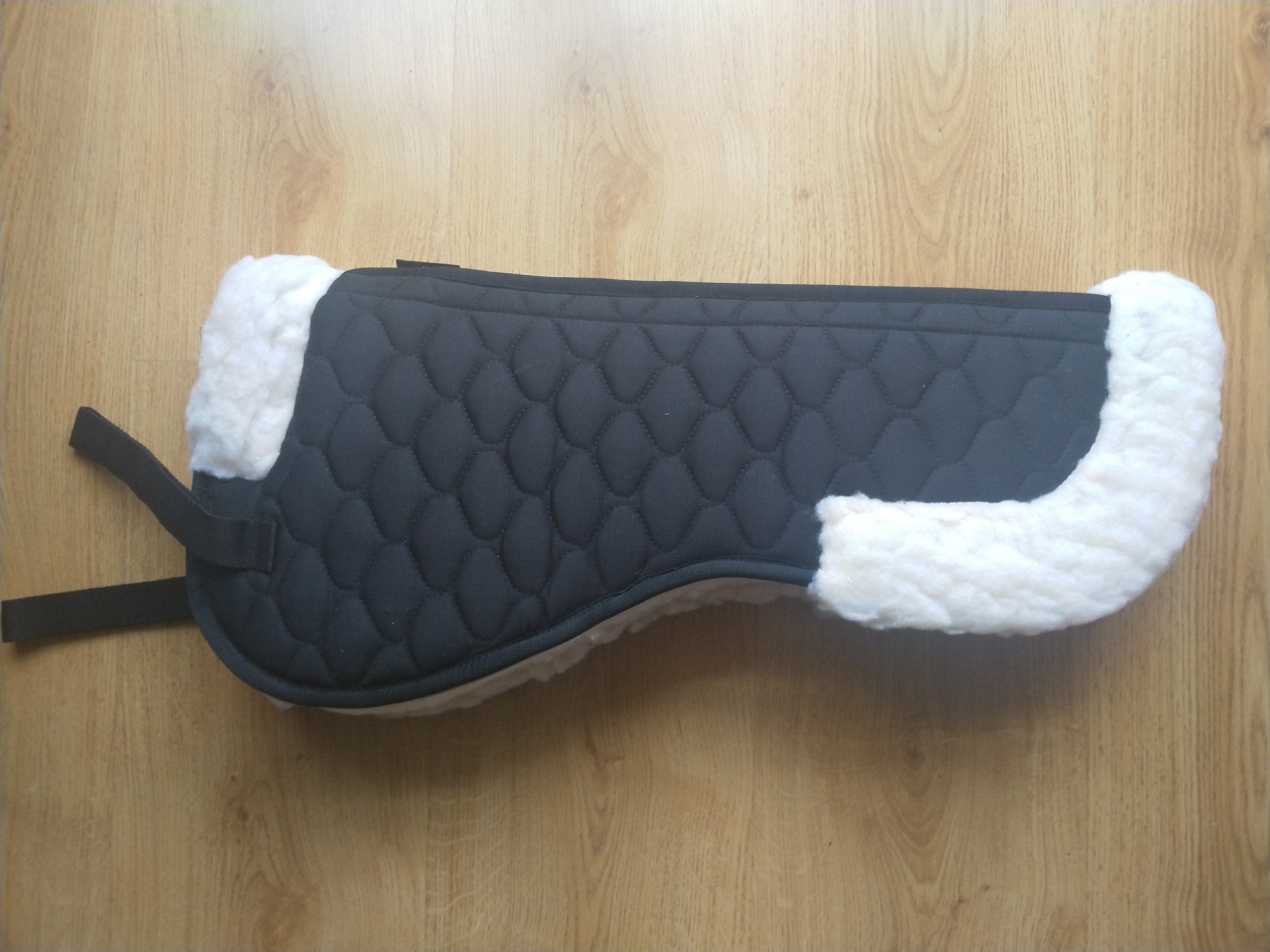 Protector de sela preto acolchoado com bordas brancas felpudas sobre chão de madeira