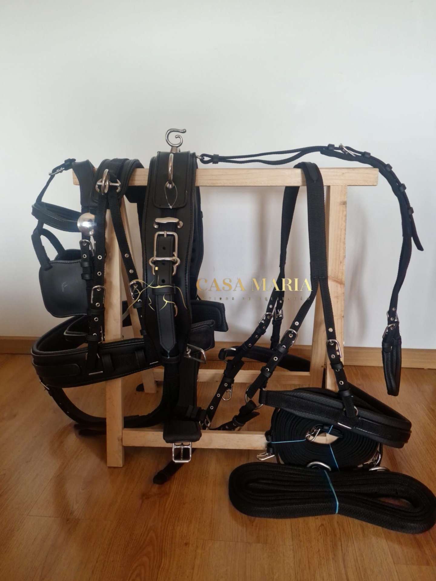 Conjunto de cabresto e arreios de couro preto com fivelas prateadas sobre estrutura de madeira