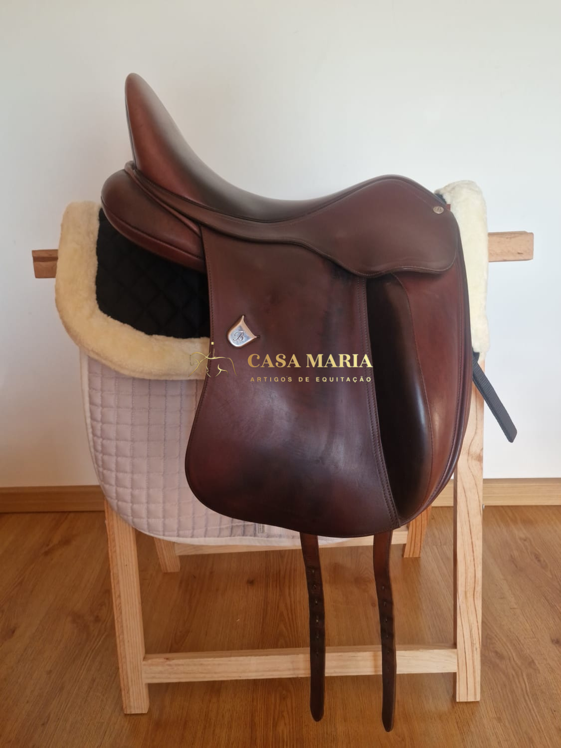 Sela de equitação castanha escura sobre suporte de madeira com almofada preta e branca