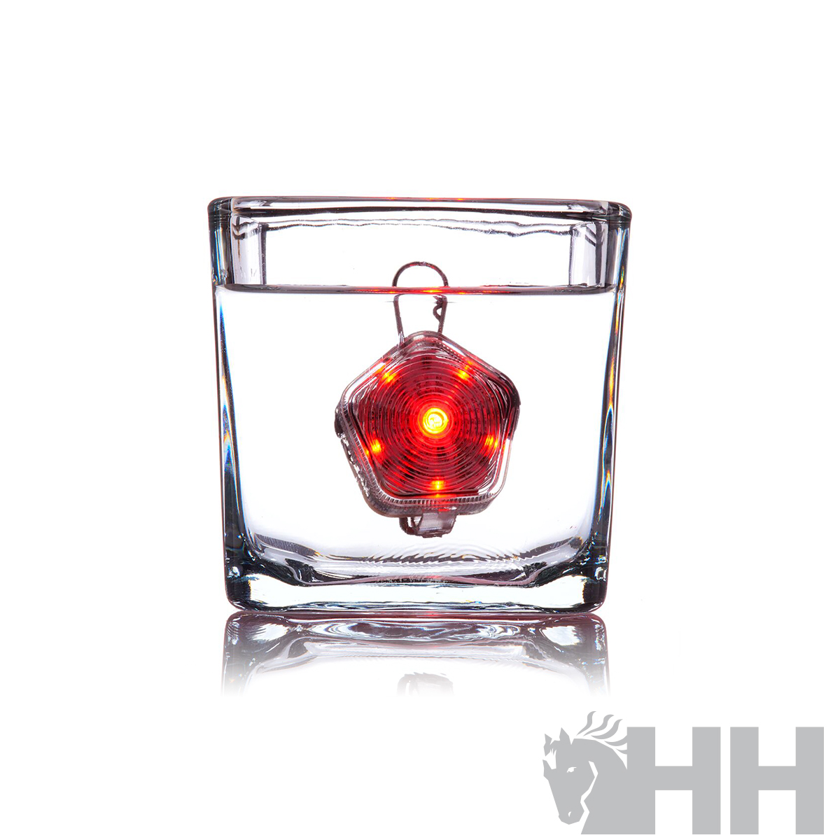 Objeto metálico pentágono com LEDs vermelhos dentro de copo de vidro transparente cheio de água