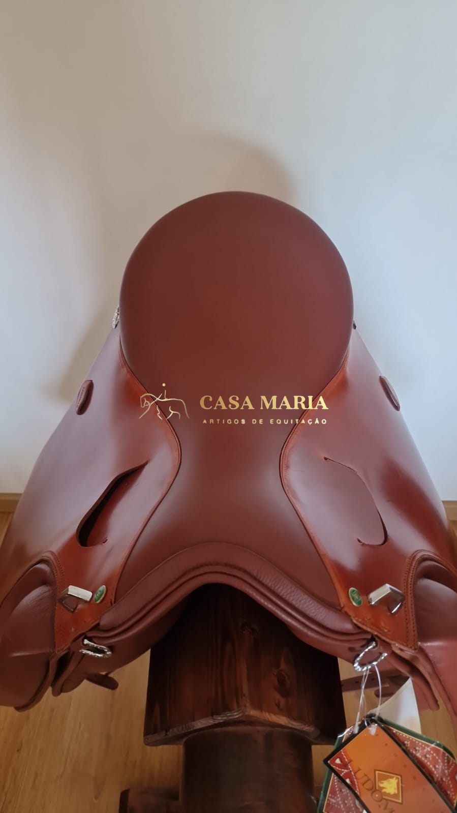 Selim de equitação em pele castanha com fivelas metálicas e suporte de madeira