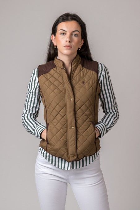 Colete acolchoado castanho feminino com detalhes castanhos escuros, usado com camisa riscada verde e branca e calças brancas