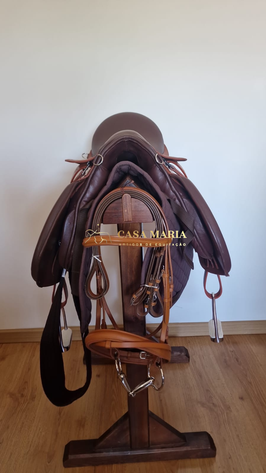 Selim de equitação castanho com estribos, montado em suporte de madeira