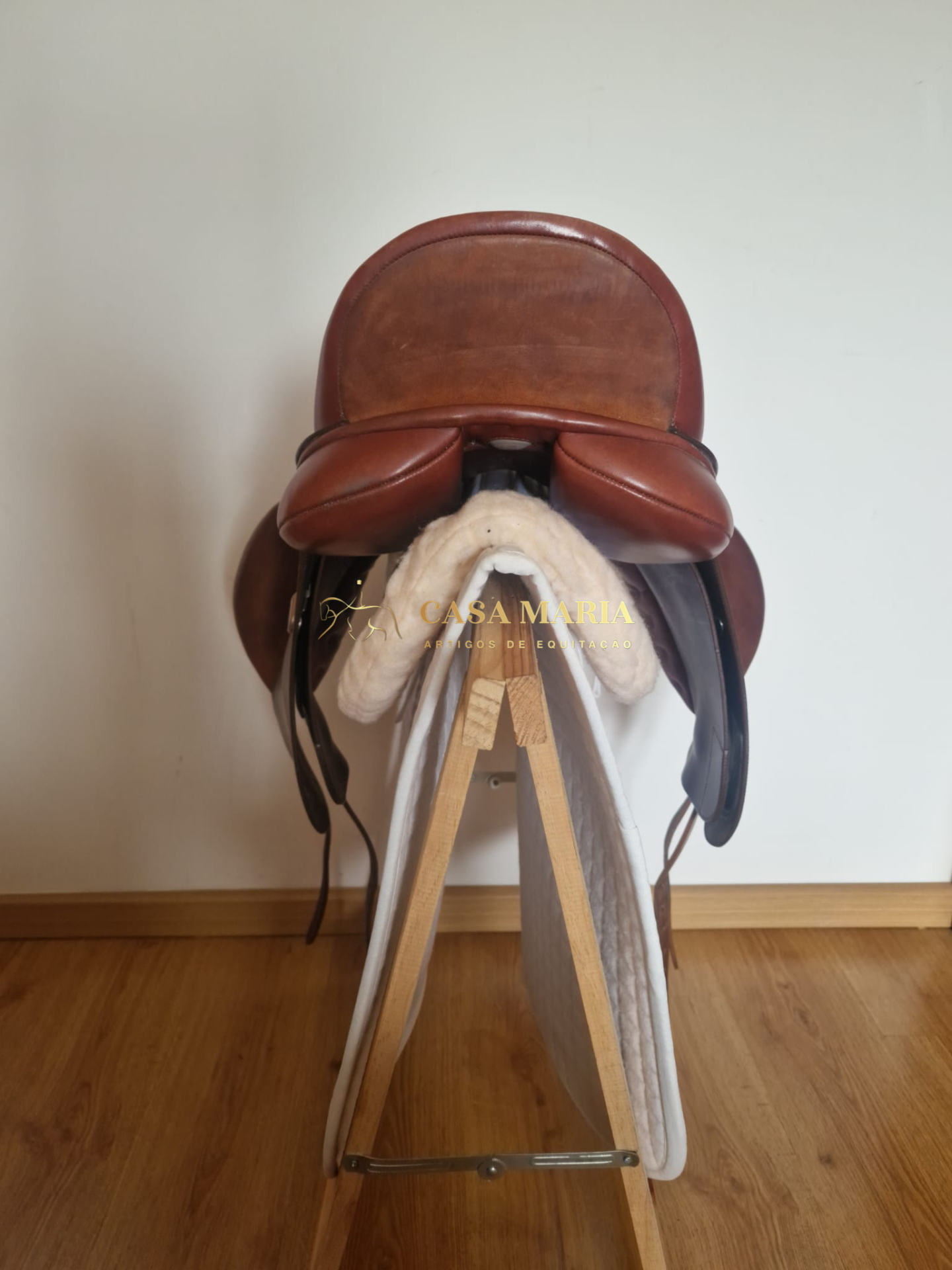 Sela de equitação em couro castanho sobre suporte de madeira