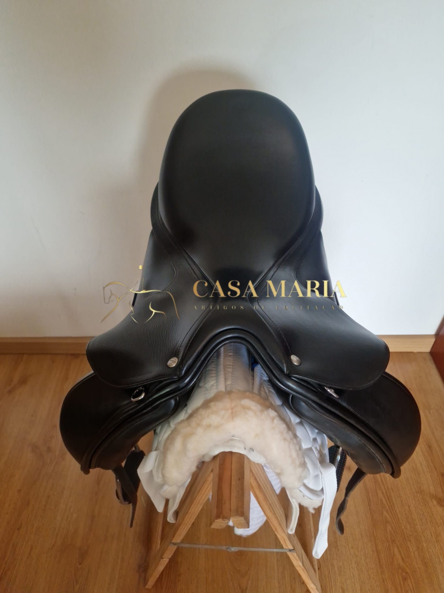Sela de equitação preta em couro num suporte de madeira com acolchoamento branco.