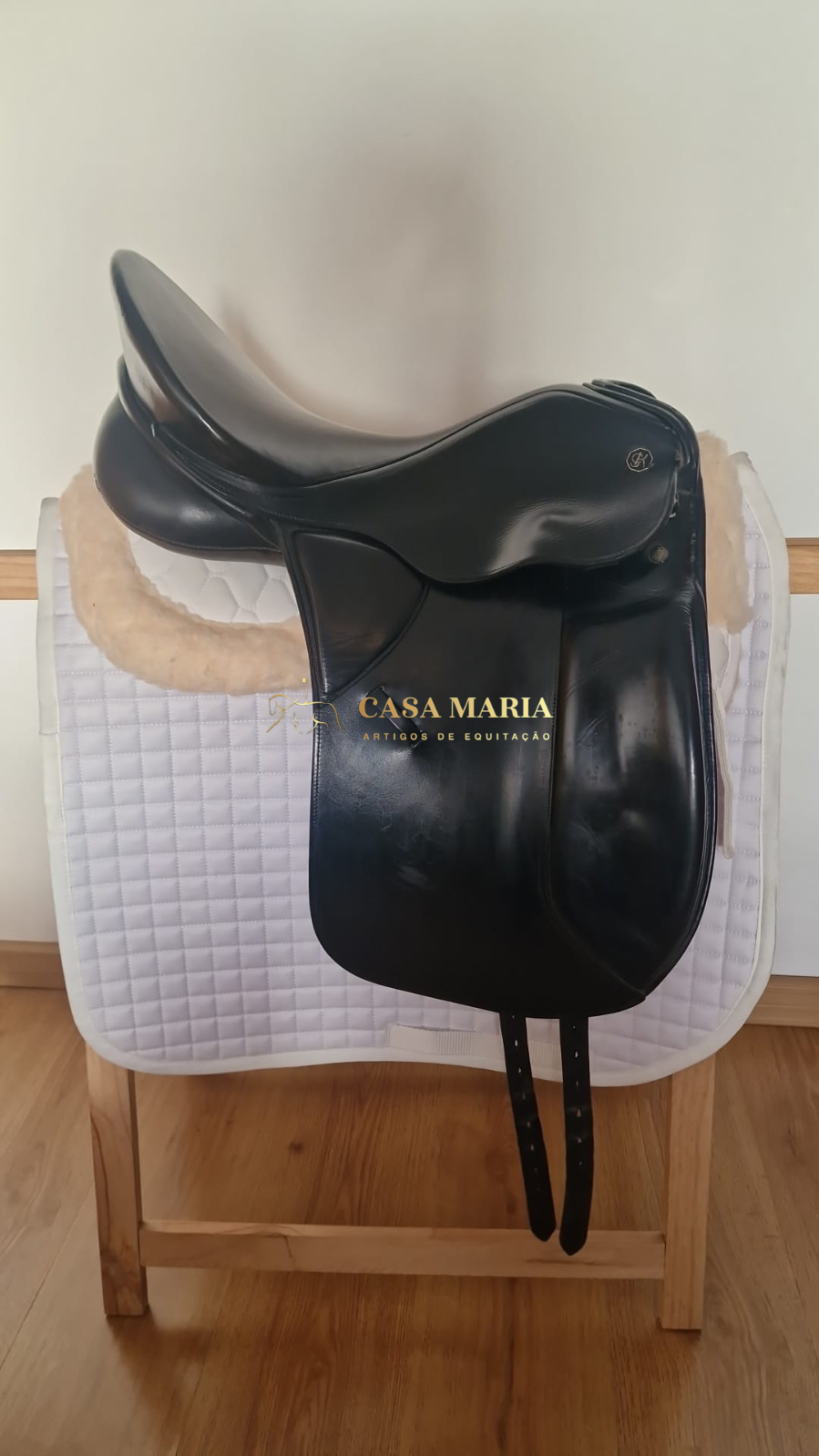 Sela preta de couro sobre manta branca em suporte de madeira