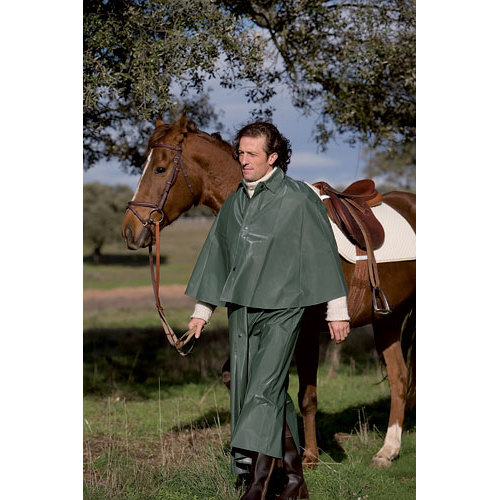 Homem com capa e calças impermeáveis verdes segurando rédea de cavalo castanho com sela branca e castanha em área gramada