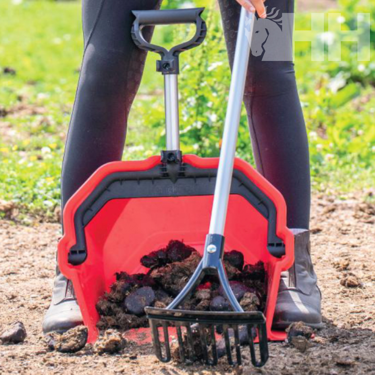 Recipiente vermelho e preto com cabo metálico para recolher estrume num jardim