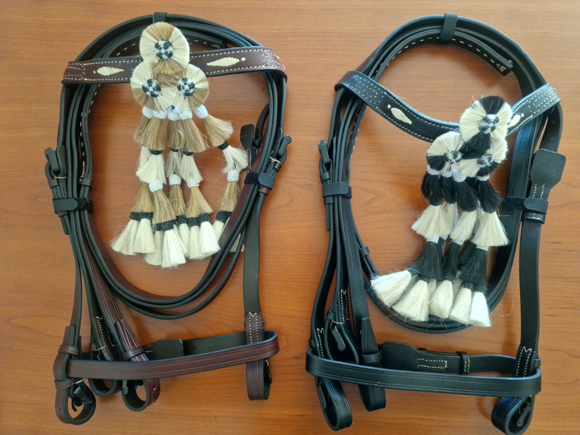 Duas rédeas de couro com enfeites de tecido pretos e brancos sobre madeira