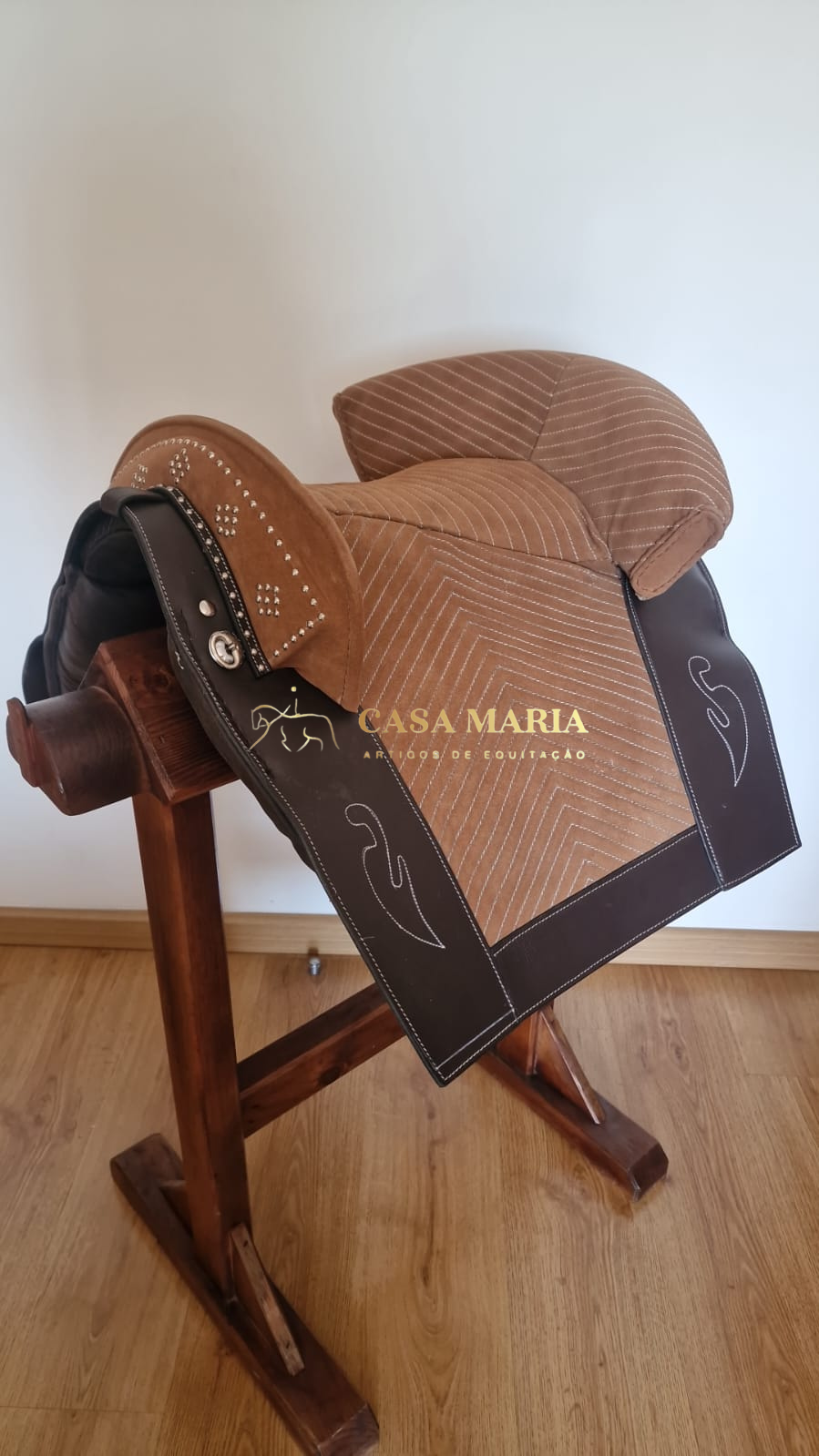 Sela de equitação castanha e bege com detalhes em couro escuro e suporte de madeira