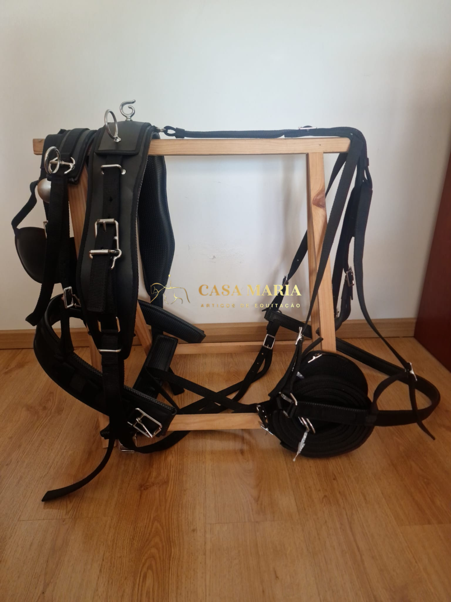 Cabresto e rédea pretos com fivelas metálicas pendurados num suporte de madeira clara