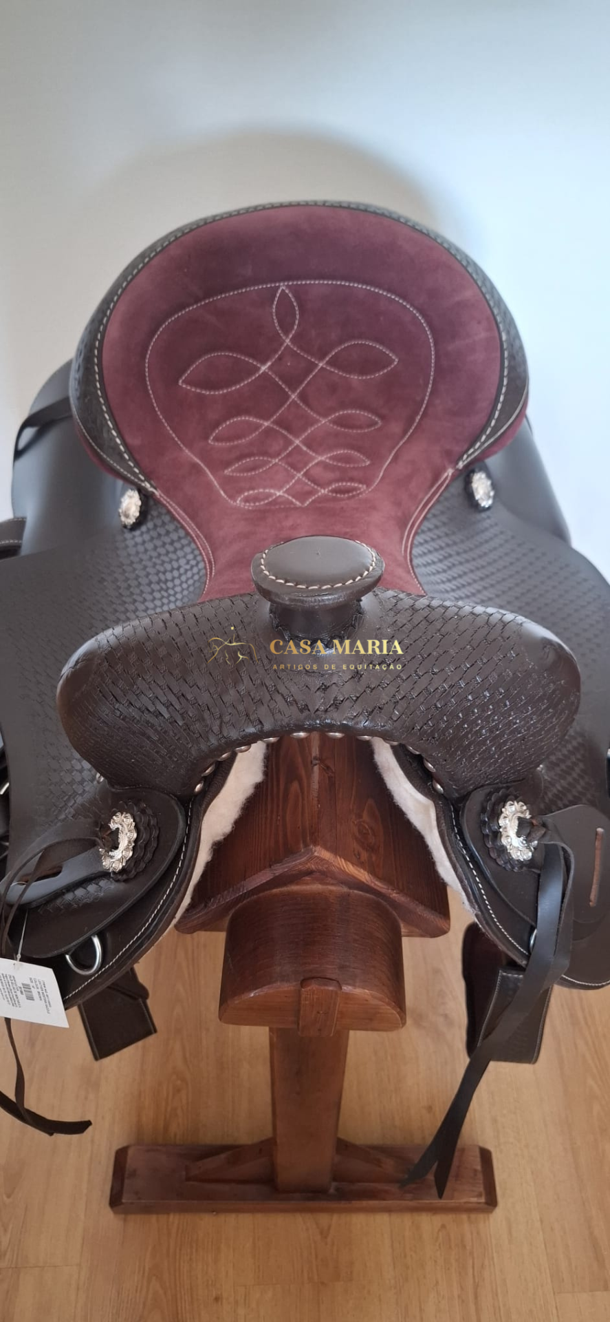Sela de equitação em camurça roxa e couro castanho com detalhes prateados sobre suporte de madeira